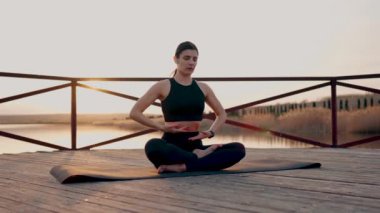 Genç kadın meditasyon yapıyor ve gün batımında göl kenarında yoga egzersizleri yapıyor. Yoga ve zindelik kavramı. Yoga asanas.