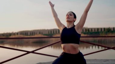 Genç kadın meditasyon yapıyor ve gün batımında göl kenarında yoga egzersizleri yapıyor. Yoga ve zindelik kavramı. Yoga asanas.
