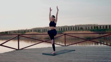 Genç kadın meditasyon yapıyor ve gün batımında göl kenarında yoga egzersizleri yapıyor. Yoga ve zindelik kavramı. Yoga asanas.