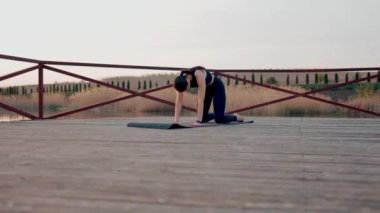 Genç kadın meditasyon yapıyor ve gün batımında göl kenarında yoga egzersizleri yapıyor. Yoga ve zindelik kavramı. Yoga asanas.