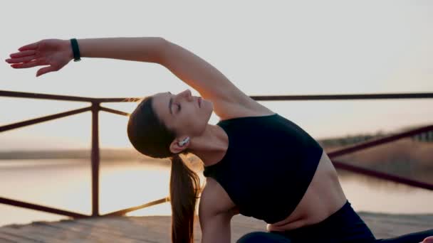 若い女性は日没で湖のエンバンクメントで瞑想し ヨガ演習を行います ヨガとフィットネスコンセプト ヨガアサナ — ストック動画