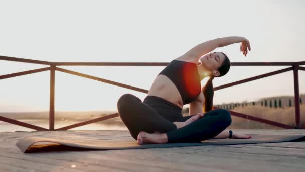 若い女性は日没で湖のエンバンクメントで瞑想し ヨガ演習を行います ヨガとフィットネスコンセプト ヨガアサナ — ストック動画