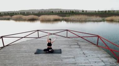 Genç kadın meditasyon yapıyor ve gün batımında göl kenarında yoga egzersizleri yapıyor. Yoga ve zindelik kavramı. Yoga.