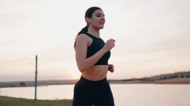 Spor giyimli genç bir kadın gün batımında setin yanında koşuyor. Sağlıklı yaşam tarzı kavramı