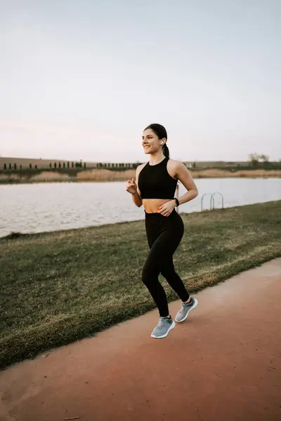 Spor giyimli genç bir kadın gün batımında setin yanında koşuyor. Sağlıklı yaşam tarzı kavramı