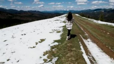 Mutlu bir kadın kar kaplı dağların tepesinde koşar ve dans eder. Seyahat konsepti. 4k İHA atışı