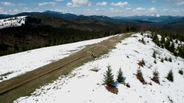 Mutlu bir kadın kar kaplı dağların tepesinde koşar ve dans eder. Seyahat konsepti. 4k İHA atışı