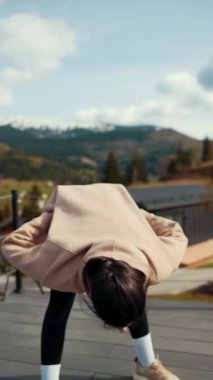 Genç bir kadın, karlı dağlara bakan bir otelin terasında sabah egzersizleri yapıyor. Sağlıklı yaşam tarzı kavramı. Dikey video