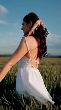 Beyaz elbiseli güzel bir kadın yeşil buğday tarlasında poz veriyor ve dans ediyor. Özgürlük kavramı. Dikey video