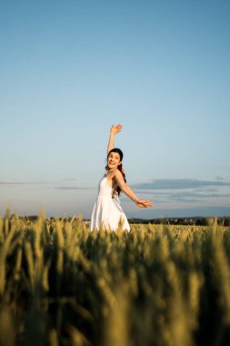 Beyaz elbiseli güzel bir kadın yeşil buğday tarlasında poz veriyor ve dans ediyor. Özgürlük kavramı. Yeşil buğday tarlasında fotoğraf çekimi.