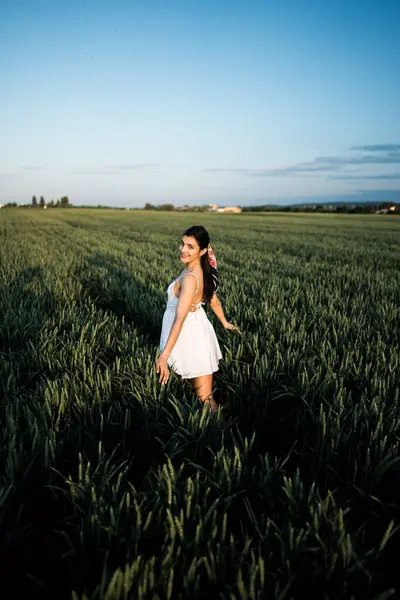 stock image Beautiful woman in a white dress posing and dancing in a green wheat field. Freedom concept.Photo session in a green wheat field