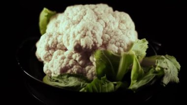 Çiğ karnabahar siyah arka planda bir tabakta dönüyor. Sebze konsepti 4k