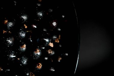 Siyah frenk üzümü siyah bir arka planda bir tabakta dönüyor. Meyve konsepti 4K