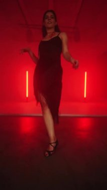 Siyah elbiseli seksi kadın kırmızı neon ışıkta Latince dans ediyor. Dans ve koreografi kavramı. Dikey video 4k