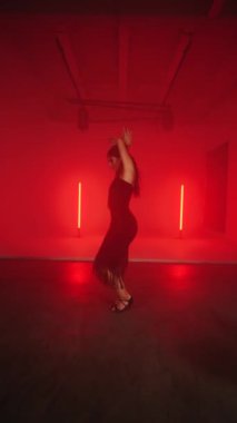Siyah elbiseli seksi kadın kırmızı neon ışıkta Latince dans ediyor. Dans ve koreografi kavramı. Dikey video 4k