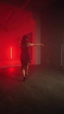 Siyah elbiseli seksi kadın kırmızı neon ışıkta Latince dans ediyor. Dans ve koreografi kavramı. Dikey video 4k