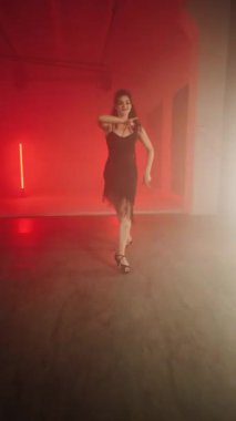 Siyah elbiseli seksi kadın kırmızı neon ışıkta Latince dans ediyor. Dans ve koreografi kavramı. Dikey video 4k