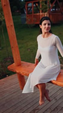 Beyaz elbiseli genç bir kadın gün batımında dağlarda büyük bir salıncakta sallanıyor. Özgürlük ve seyahat kavramı. Dikey video