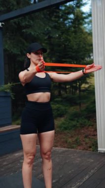 Atletik kadın ormanın yakınındaki terasta elastik bantlarla egzersiz yapıyor. Spor ve spor konsepti. Dikey video