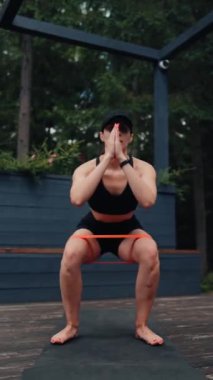 Atletik kadın ormanın yakınındaki terasta elastik bantlarla egzersiz yapıyor. Spor ve spor konsepti. Dikey video