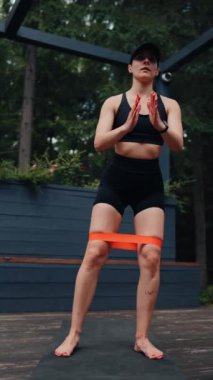 Atletik kadın ormanın yakınındaki terasta elastik bantlarla egzersiz yapıyor. Spor ve spor konsepti. Dikey video