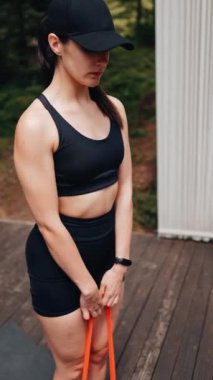 Atletik kadın ormanın yakınındaki terasta elastik bantlarla egzersiz yapıyor. Spor ve spor konsepti. Dikey video
