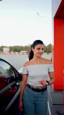Bir kadın benzin istasyonunda bir arabaya benzin dolduruyor. Benzin istasyonu servisi. Yakıt ikmali konsepti. Dikey video 4k