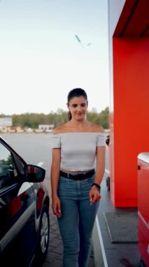 Bir kadın benzin istasyonunda bir arabaya benzin dolduruyor. Benzin istasyonu servisi. Yakıt ikmali konsepti. Dikey video 4k