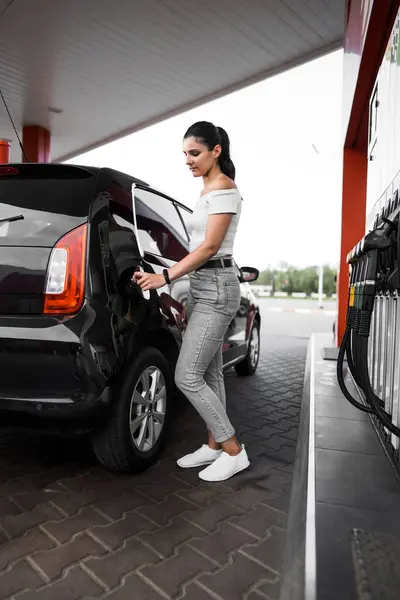 Bir kadın benzin istasyonunda bir arabaya benzin dolduruyor. Benzin istasyonu servisi. Yakıt doldurma kavramı. 