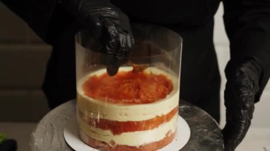 Bir kadın pasta şefi mango tutkulu meyveli pasta hazırlıyor. Pasta şefi pastaya krema sürüyor. Pasta şefi pastanın katmanlarını topluyor..