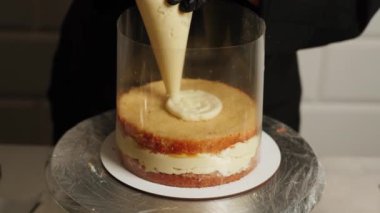 Bir kadın pasta şefi mango tutkulu meyveli pasta hazırlıyor. Pasta şefi pastaya krema sürüyor. Pasta şefi pastanın katmanlarını topluyor..