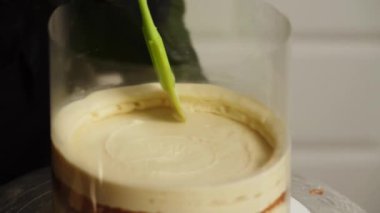 Bir kadın pasta şefi mango tutkulu meyveli pasta hazırlıyor. Pasta şefi pastaya krema sürüyor. Pasta şefi pastanın katmanlarını topluyor..
