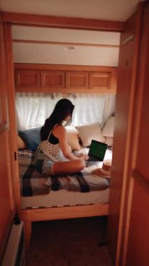 Serbest çalışan bir kadın karavanda seyahat ederken dizüstü bilgisayarda çalışıyor. Laptopta yeşil ekran. Uzaktan çalışma konsepti. Tatilde çalışıyorum. Dikey video