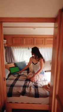 Serbest çalışan bir kadın karavanda seyahat ederken dizüstü bilgisayarda çalışıyor. Laptopta yeşil ekran. Uzaktan çalışma konsepti. Tatilde çalışıyorum. Dikey video