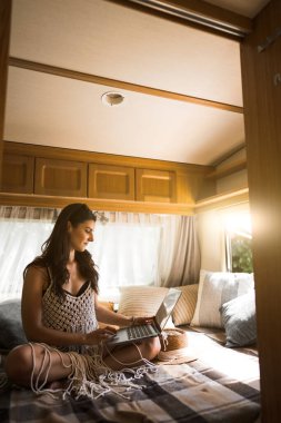 Freelancer seyahat ederken bir dizüstü bilgisayarda çalışır. Doğadaki bir karavanda dizüstü bilgisayarla çalışan bir kadın. Uzak çalışma konsepti