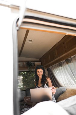 Freelancer seyahat ederken bir dizüstü bilgisayarda çalışır. Doğadaki bir karavanda dizüstü bilgisayarla çalışan bir kadın. Uzak çalışma konsepti