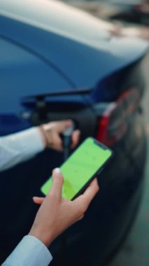 Genç bir kadın bir süpermarketin yakınındaki şarj istasyonunda bir arabayı şarj ediyor. Elektrikli bir arabayı şarj etmek. Elektrikli araba konsepti. Dikey video