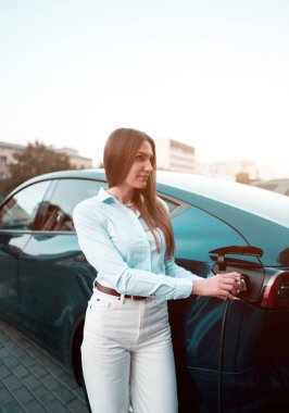 Genç bir kadın bir süpermarketin yakınındaki şarj istasyonunda bir arabayı şarj ediyor. Elektrikli bir arabayı şarj etmek. Elektrikli araba konsepti. Dikey fotoğraf