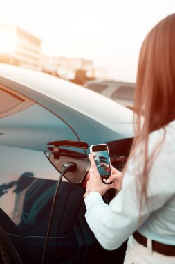 Genç bir kadın bir süpermarketin yakınındaki şarj istasyonunda bir arabayı şarj ediyor. Elektrikli bir arabayı şarj etmek. Elektrikli araba konsepti. Dikey fotoğraf