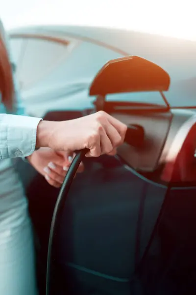 stock image A young woman charges a car at a charging station near a supermarket. Charging an electric car. Electric car concept. Vertical photo