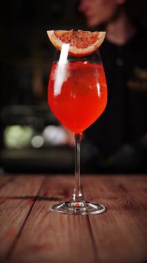 Barmen bir kulüpte kokteyl hazırlıyor. Barmen bir kokteylin içine buz atıp meyve suyu döker. Alkolik kokteyl konsepti. Dikey video