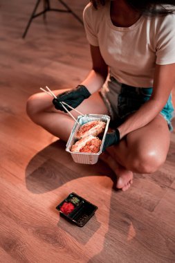 Lotus pozisyonunda otururken yemek çubuklarıyla suşi burger yiyen genç bir kadın. Japon yemeği konsepti. Ellerinde suşi burgeri