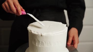 Pastanın kenarlarını düzleştirme süreci. Pasta şefi pastaya krema sürüyor ve spatula kullanarak pastanın kenarlarını düzleştiriyor. Pasta ve pasta konsepti