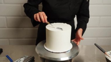 Pastanın kenarlarını düzleştirme süreci. Pasta şefi pastaya krema sürüyor ve spatula kullanarak pastanın kenarlarını düzleştiriyor. Pasta ve pasta konsepti