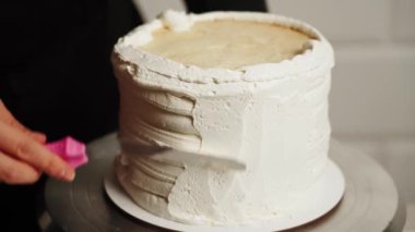 Pastanın kenarlarını düzleştirme süreci. Pasta şefi pastaya krema sürüyor ve spatula kullanarak pastanın kenarlarını düzleştiriyor. Pasta ve pasta konsepti