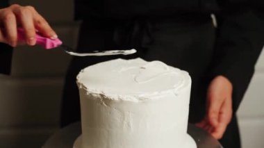 Pastanın kenarlarını düzleştirme süreci. Pasta şefi pastaya krema sürüyor ve spatula kullanarak pastanın kenarlarını düzleştiriyor. Pasta ve pasta konsepti
