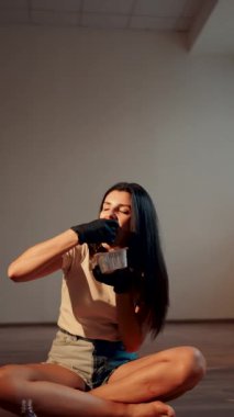 Lotus pozisyonunda otururken yemek çubuklarıyla suşi burger yiyen genç bir kadın. Japon yemeği konsepti. Ellerinde suşi burgeri. Dikey Vedeo 4K.
