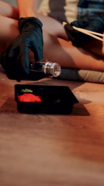 Lotus pozisyonunda otururken yemek çubuklarıyla suşi burger yiyen genç bir kadın. Japon yemeği konsepti. Ellerinde suşi burgeri. Dikey Vedeo 4K.