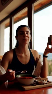 Genç bir kadın, pencereden dağları gören bir restoranda ekmekle pancar çorbası yiyor. Ukrayna mutfağı konsepti. Kırmızı borş çorbası. Dikey video