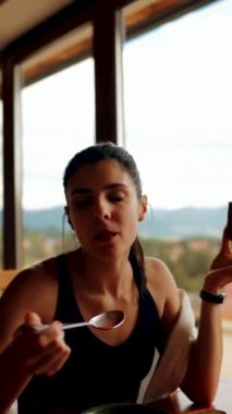 Genç bir kadın, pencereden dağları gören bir restoranda ekmekle pancar çorbası yiyor. Ukrayna mutfağı konsepti. Kırmızı borş çorbası. Dikey video